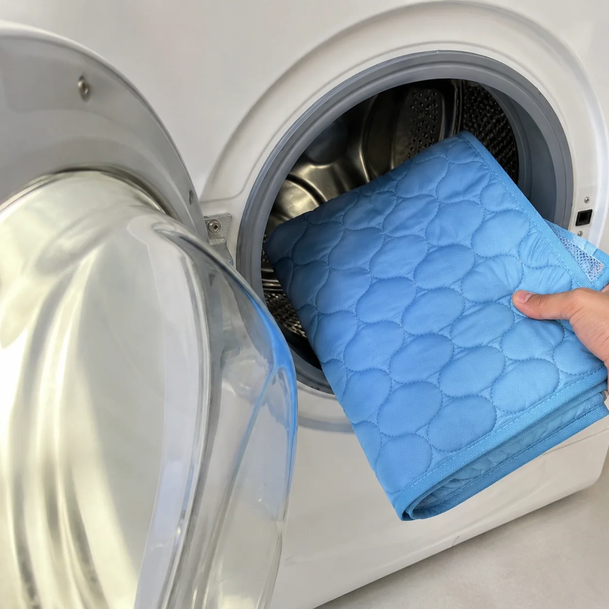 Tapete gelado azul dobrado sendo colocado no tambor da máquina de lavar
